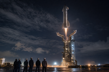 Starship upper stage descending toward launch tower catch arms at night with illuminated tower and distant engineers