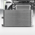 A silver metallic automotive radiator shown from the front, with a blurred background of a car engine bay.