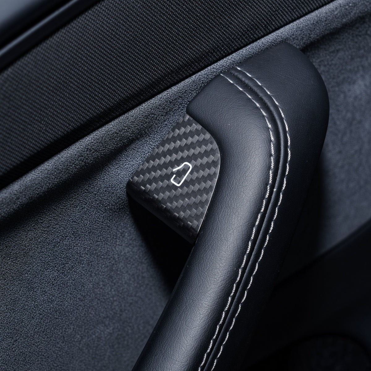 Carbon-weave door-release cover fitted beside the stitched edge of a black door grab handle.