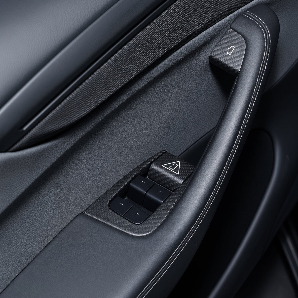 Black door panel with carbon-weave trim around four window switches and covers at the door-release controls.