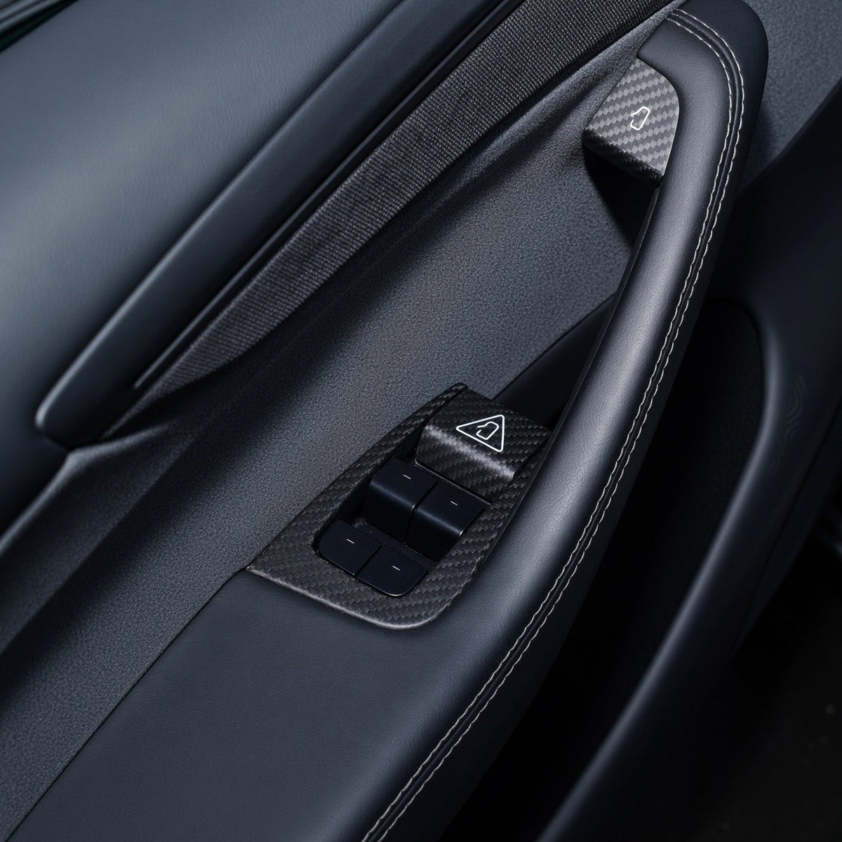Door-panel overview showing carbon-weave covers on the four-switch surround and the upper door-release area.
