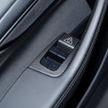 Angled view of a carbon-weave surround and triangular release-button cover around four black window switches.