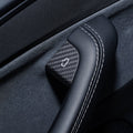 Carbon-weave door-release cover fitted beside the stitched edge of a black door grab handle.
