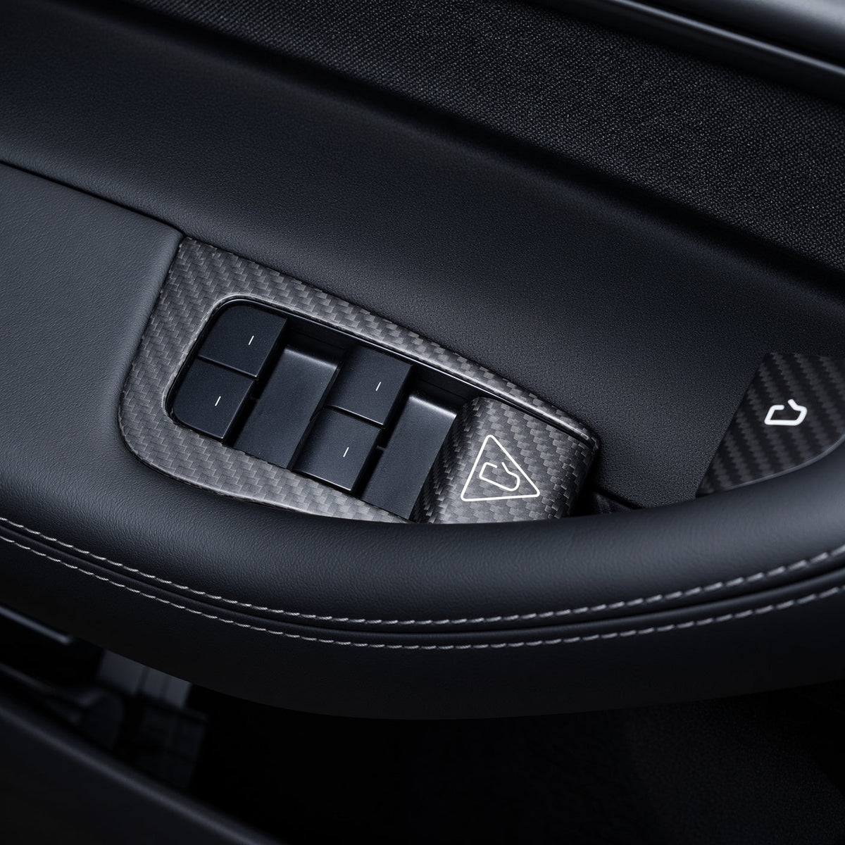 Carbon-weave driver-door switch surround viewed across the grab handle, showing four window switches and release-button covers.