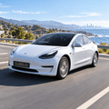 White Model 3 on a coastal road with a black front license plate bracket fitted